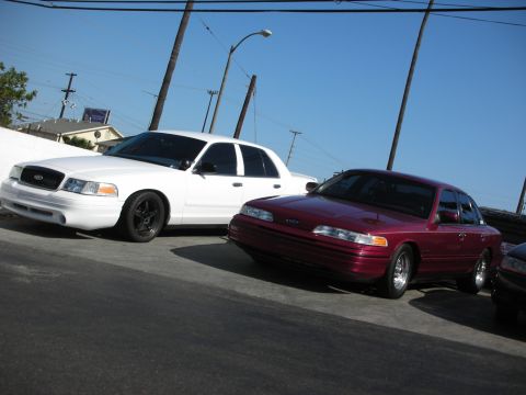 1992 Ford Crown Victoria - Two Ford Crown Victorias are parked on a street under a clear blue sky.