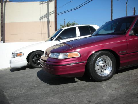 1992 Ford Crown Victoria - Two Ford Crown Victorias, one maroon and one white, are parked next to each other on a sunny day.