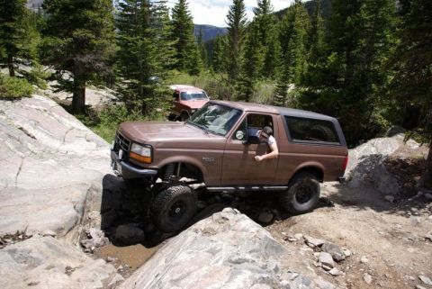 1993 Ford Bronco - 1993 Ford Bronco tackling a challenging off-road course in a wooded mountain area.