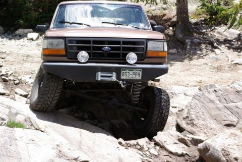1993 Ford Bronco - This Ford Bronco is tackling a difficult off-road trail, with one wheel significantly elevated.