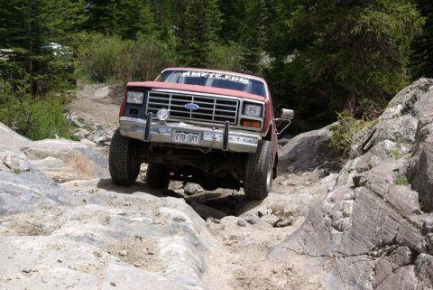 1993 Ford Bronco - This red Ford Bronco is shown tackling a challenging rocky terrain on a mountain trail.