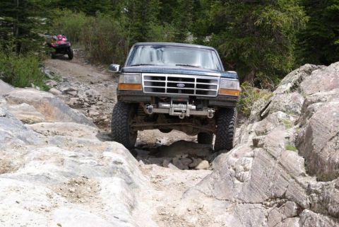 1993 Ford Bronco - A 1993 Ford Bronco navigates a rocky off-road trail, with an ATV following in the background.