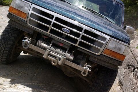1993 Ford Bronco - A dark green 1993 Ford Bronco navigates a rocky trail, its front grille and winch clearly visible.