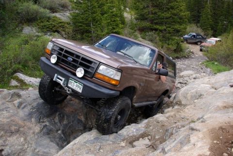 1993 Ford Bronco - 1993 Ford Bronco tackling a challenging off-road course on a mountain trail.