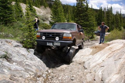 1993 Ford Bronco - A brown Ford Bronco tackles a challenging rocky path with a photographer nearby.
