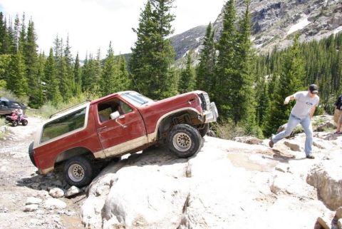 1993 Ford Bronco - A red SUV navigates a challenging rocky trail with a person running alongside.