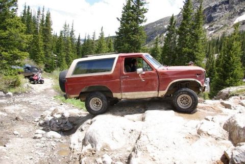 1993 Ford Bronco - This red Ford Bronco navigates a challenging rocky trail, with an ATV and another SUV visible further up the path.
