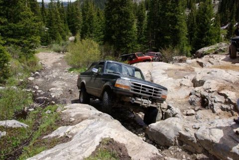 1993 Ford Bronco - A modified Ford Bronco tackles a challenging rocky trail in a mountainous, forested area.