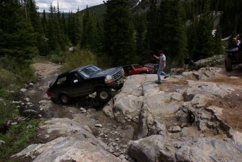 1993 Ford Bronco - A black 1992 Ford Bronco tackles a challenging rocky terrain on a mountain path with other vehicles visible in the background.