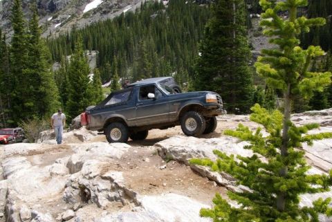 1993 Ford Bronco - This Ford Bronco is navigating a challenging rocky trail in a mountainous, forested area.