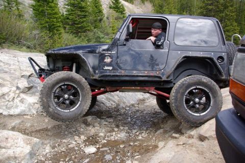 1993 Ford Bronco - Modified Jeep Wrangler TJ tackling a challenging off-road trail with a driver inside.