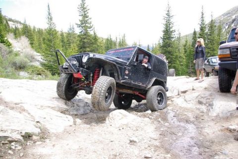 1993 Ford Bronco - A modified Jeep navigates a rocky off-road course with trees and mountains in the background.