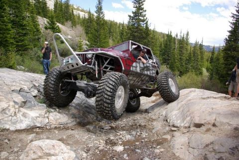 1993 Ford Bronco - A heavily modified off-road vehicle navigates a rocky trail in a mountainous, forested area.
