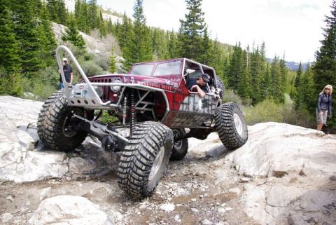 1993 Ford Bronco - This heavily modified Jeep navigates a challenging rocky trail in a mountainous, wooded area.