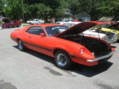 1972 Ford Ranchero - Orange 1972 Ford Ranchero GT parked at a car show, hood up, with other vehicles visible.