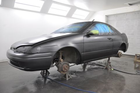1996 Ford Bronco - Car undergoing paint work in a garage, lifted on jack stands with wheels removed.