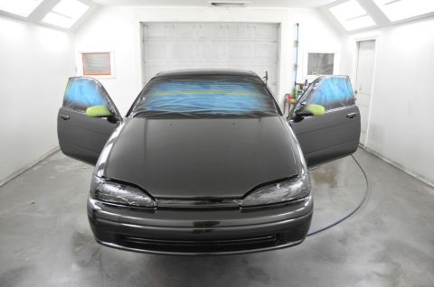 1996 Ford Bronco - A dark sedan sits in a paint booth with its doors open and windows taped off, ready for a fresh coat of paint.