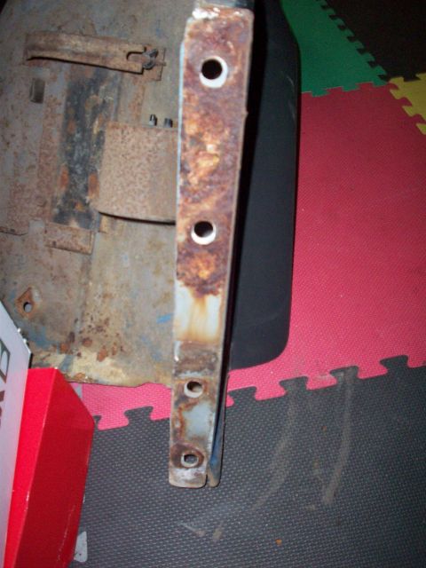 1978 Jeep CJ5 - A close-up view of a heavily rusted metal bracket with several bolt holes, suggesting it's a component from a vehicle or piece of equipment.