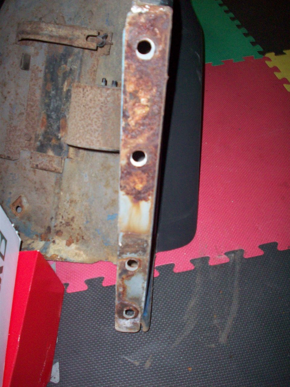 rusted metal bracket with multiple holes, part of a larger assembly