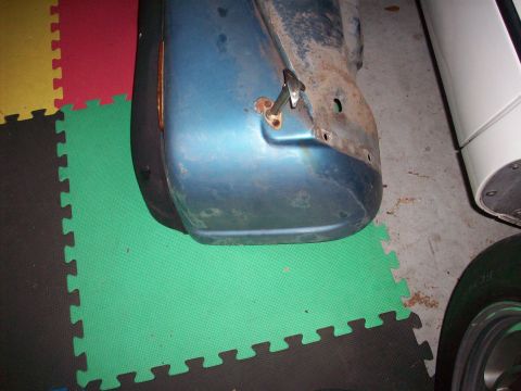1978 Jeep CJ5 - Close-up of a blue vehicle fender with visible rust and damage, resting on a multi-colored mat floor.