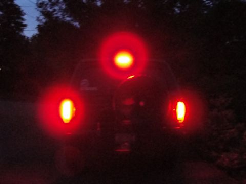1995 Ford Bronco - The rear of a dark SUV is visible at night with its tail lights and brake light illuminated.