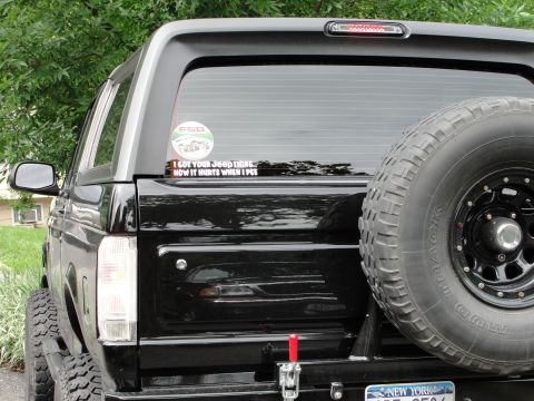 1995 Ford Bronco - Rear view of a 1995 Ford Bronco, showing a spare tire and a humorous sticker on the window.