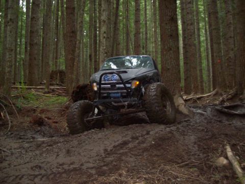1995 Ford Bronco - Off-road vehicle navigating a muddy trail through a dense forest.