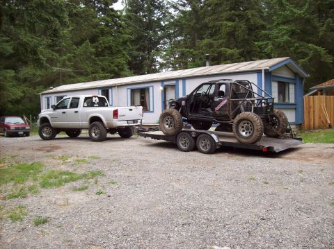 1995 Ford Bronco - A white pickup truck tows a custom off-road buggy on a trailer, with a house and trees in the background.
