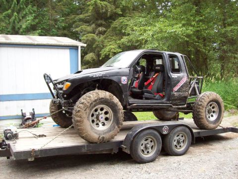 1995 Ford Bronco - Custom off-road truck with racing seats and roll cage loaded onto a trailer.