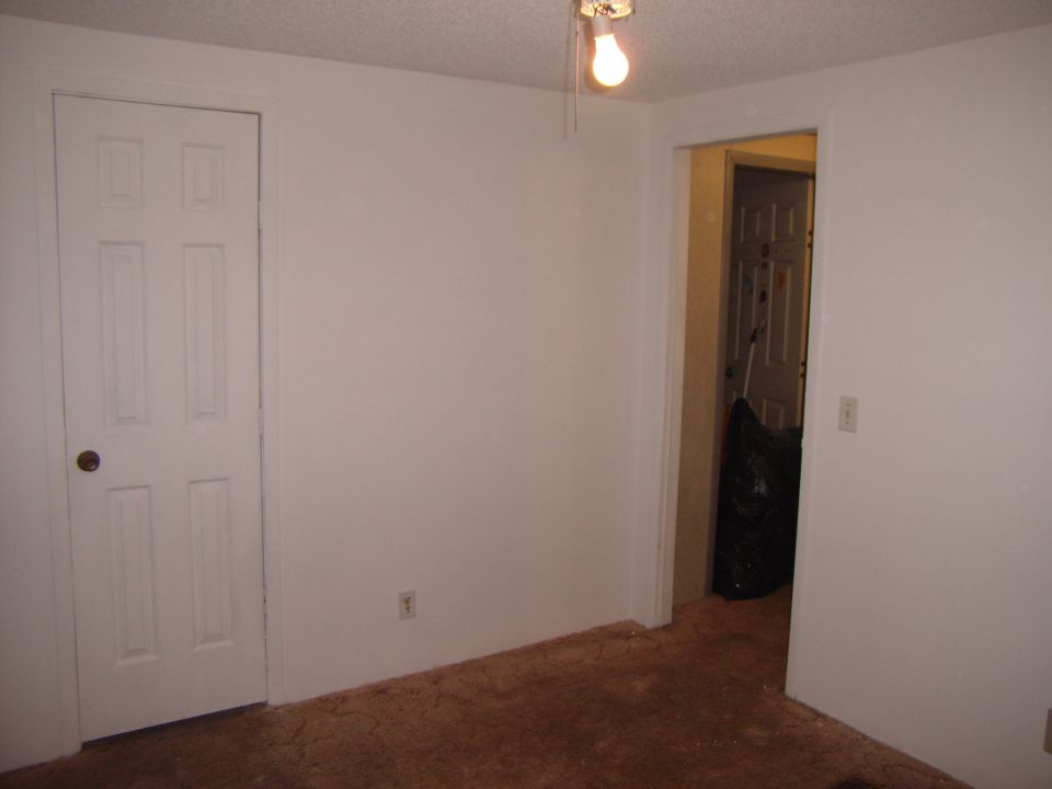 Interior room with white doors, carpet, and a light bulb. A doorway leads to another room with a trash bag