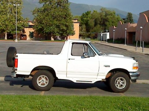 1995 Ford Bronco - A white 1995 Ford Bronco is shown from the side, parked outdoors with a spare tire on the back.