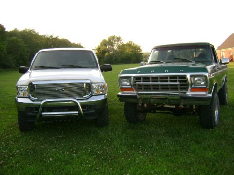 2000 Ford Excursion - Two Ford trucks, a white Excursion and a green older model, are parked side-by-side on a grassy field.