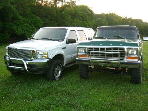 2000 Ford Excursion - Two Ford trucks, a white Excursion and a green F-Series, are parked on a grassy lawn with trees in the background.