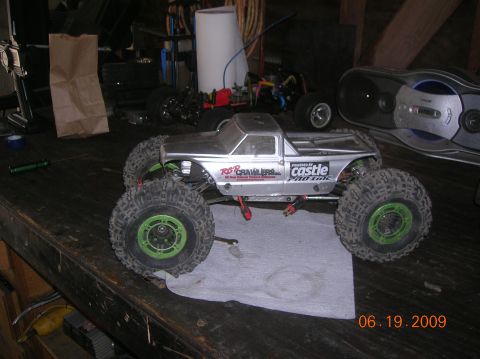 1985 Ford Bronco - RC rock crawler truck with "R2CRAWLERS.com" and "POWERED BY CASTLE" decals sits on a workbench.
