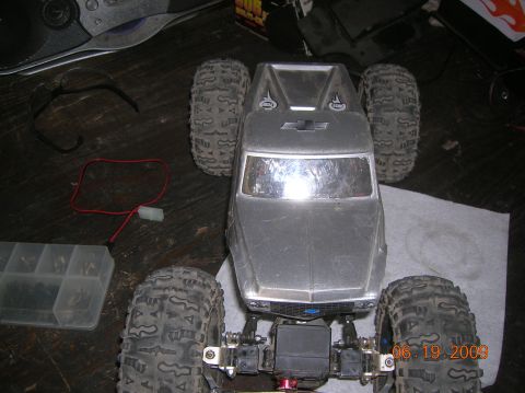 1985 Ford Bronco - A silver RC crawler truck body sits on a workbench with various electronic components and tools nearby.