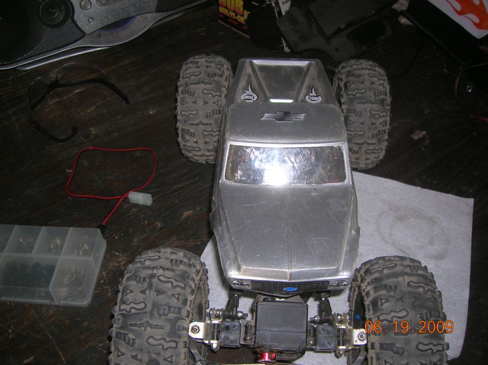 RC crawler truck body with Chevrolet emblem, large tires, and visible suspension parts
