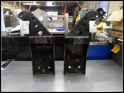 1989 Ford Bronco - Two black metal brackets are displayed on a workbench, likely for automotive use.