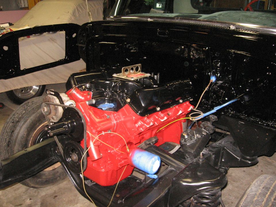 Truck engine bay with red engine, black chassis, and tire. Blue spray can visible