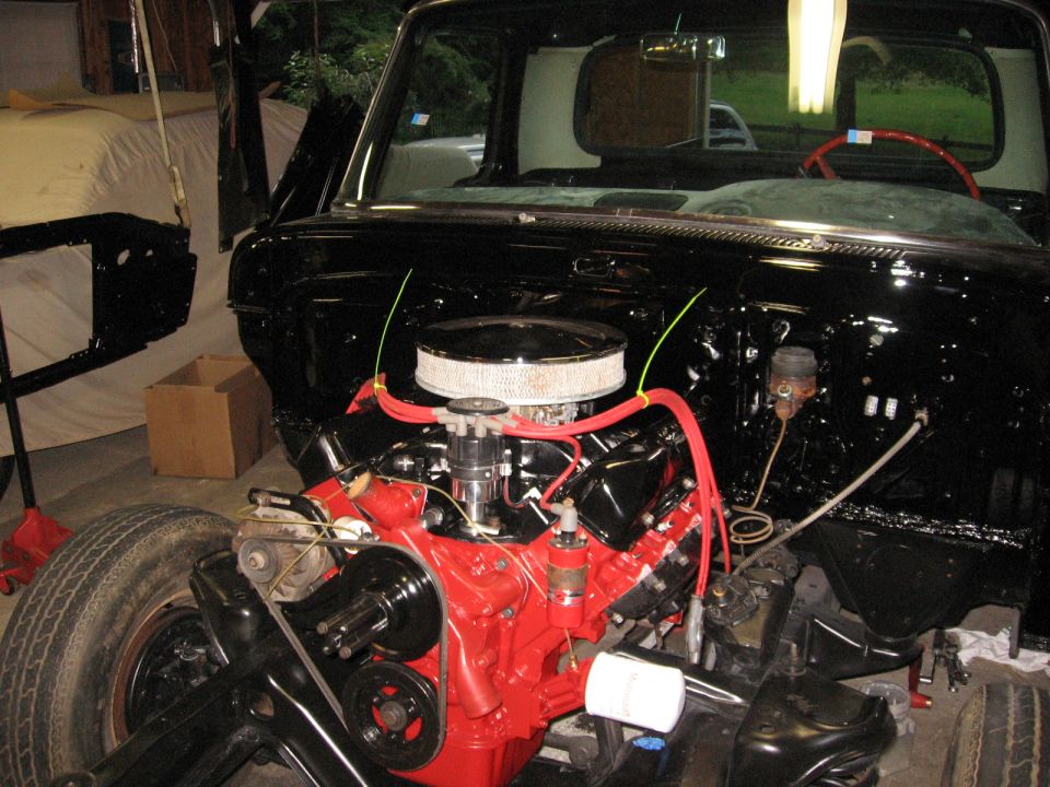 Close-up of a red V8 engine in a black classic truck's engine bay, undergoing restoration