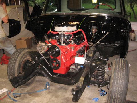 1966 Ford F-100 - A truck chassis is undergoing reassembly with a bright red engine installed.