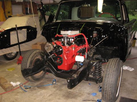 1966 Ford F-100 - A black 1966 Ford F-100 pickup truck is shown in a garage with its engine exposed, undergoing reassembly.