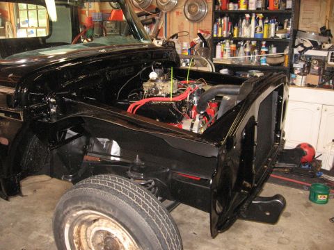 1966 Ford F-100 - Front end of a 1966 Ford F-100 undergoing restoration in a garage with shelves of supplies in the background.