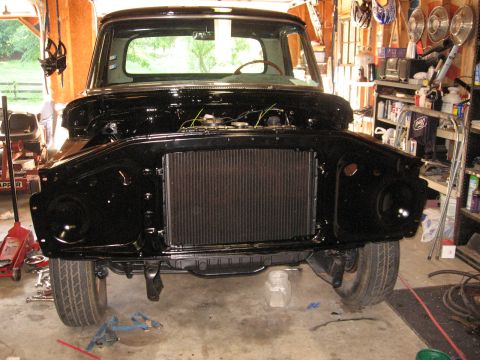 1966 Ford F-100 - This black Ford truck is undergoing reassembly in a garage, with its front end exposed.