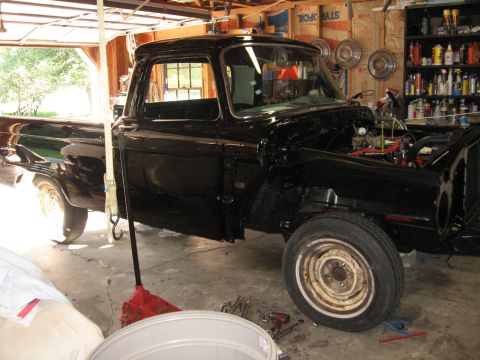 1966 Ford F-100 - A black pickup truck is undergoing repairs in a garage, with its engine compartment open and tools scattered around.