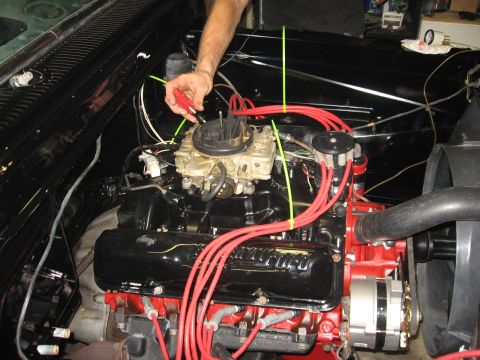 1966 Ford F-100 - A mechanic works on the engine of a vehicle, focusing on the carburetor and ignition system.