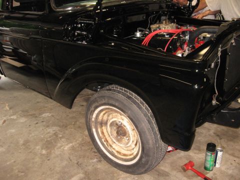 1966 Ford F-100 - A black pickup truck is undergoing work in a garage, with its hood open to reveal the engine.