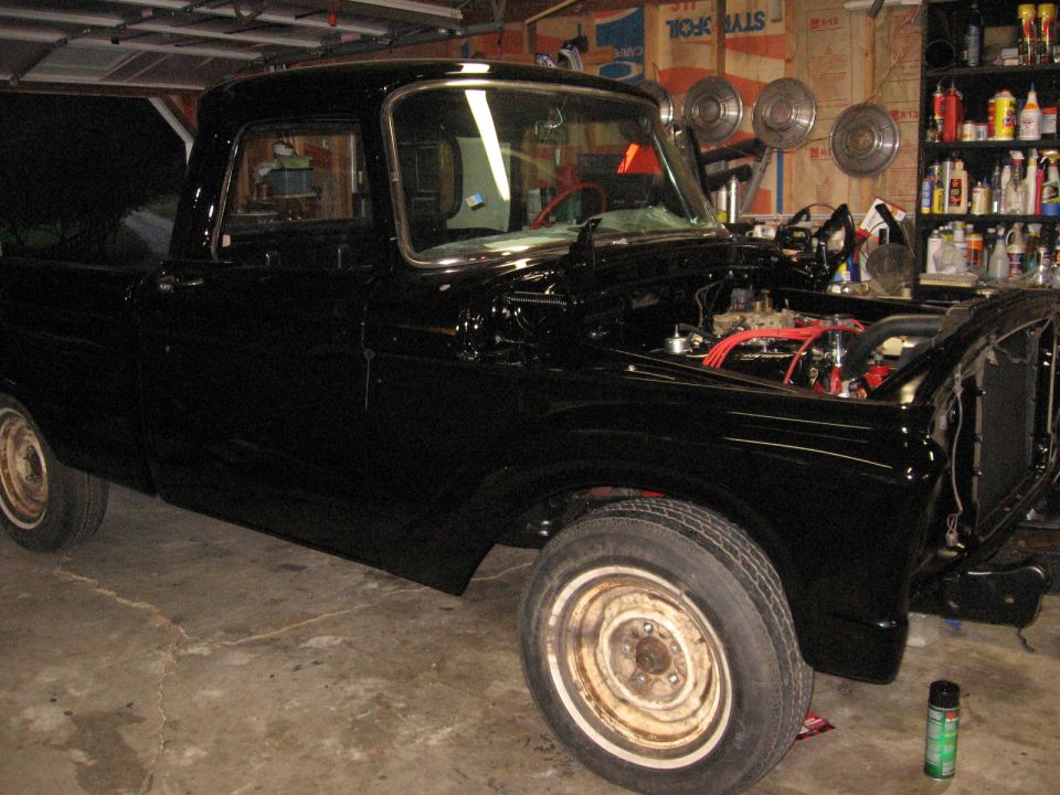 Black pickup truck with hood open, showing engine. It's in a garage with tools and parts in the background