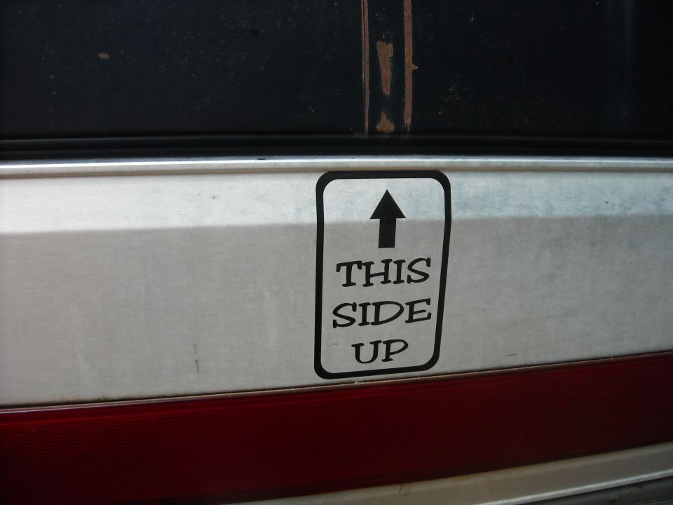 Close-up of a "THIS SIDE UP" sticker on a silver vehicle panel