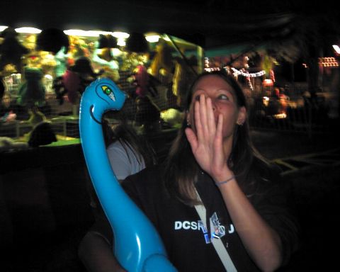 1990 Ford Taurus - Woman with inflatable dinosaur at a carnival game booth with prizes in the background.