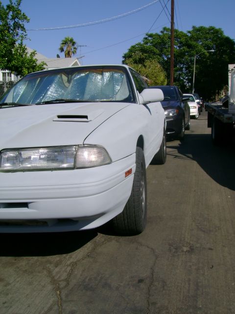 1989 Mazda MX-6 - A white Mazda MX-6 is parked on a street, with other vehicles behind it.